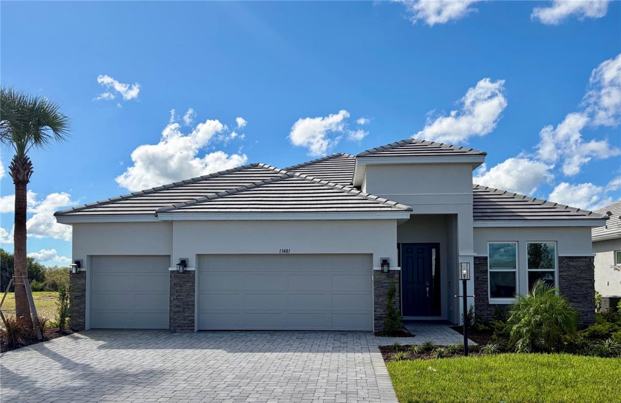 The actual Cresta at 13481 Manarola Way — the built home with its tile roof, stone accents, three-car garage and paver driveway, house number 13481 above the garage